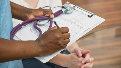 Close up of a nurse's hands holding a clipboard and stethoscope, filling in a form
