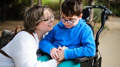 Disabled boy in a wheelchair enjoying a walk outdoors with his mother