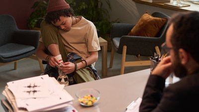 Problem schoolchild sitting in front of psychologist and tying shoelaces on his sneakers while counselor looking at him